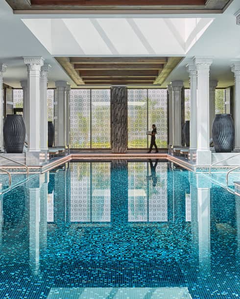Sunny indoor swimming pool lined with tall black vases, white pillars