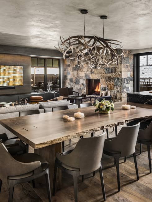 Mountain-chic dining area with wooden floors, dining table and ten leather chairs, antler chandelier