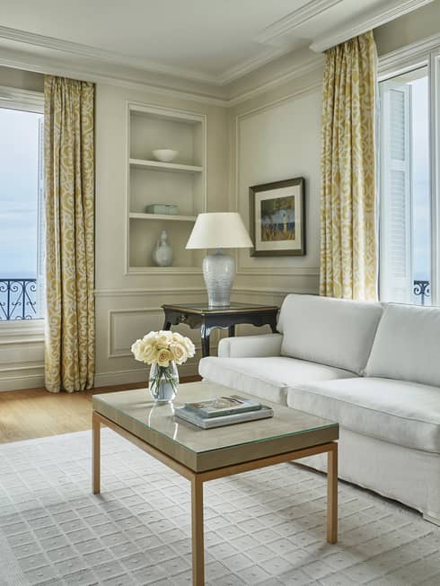 Modern white sofa, armchair, rug, table with books, flowers, corner windows
