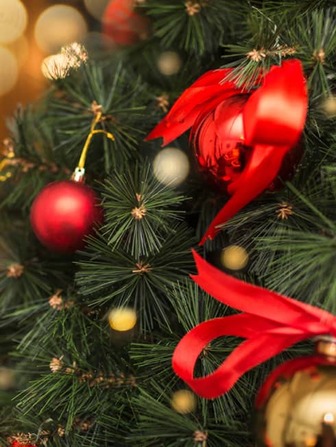 Red sphere ornaments and red ribbons on a Christmas tree.