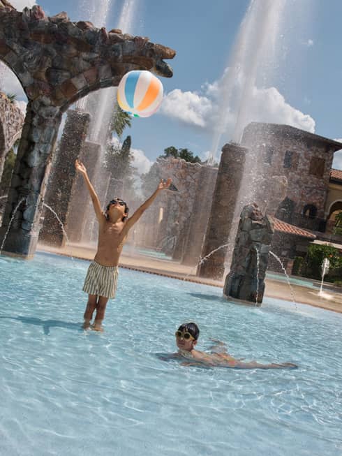 Two young guests wearing swimsuits and throwing a beach ball at the pool.
