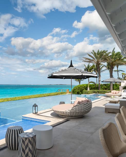 Beachfront villa residence terrace with private infinity pool, sun loungers, and ocean view under a bright blue sky