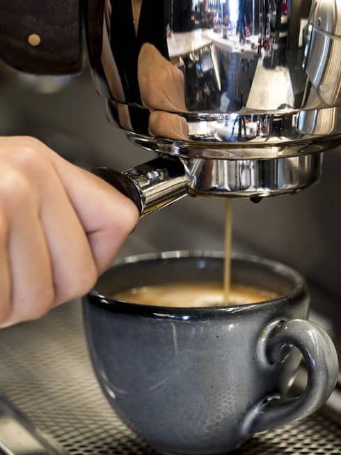 Close-up of hands pressing espresso in machine into small blue mug