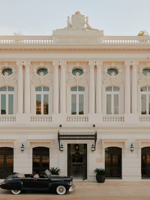 Exterior of a white stone Colonial-style hotel building with a vintage car out front