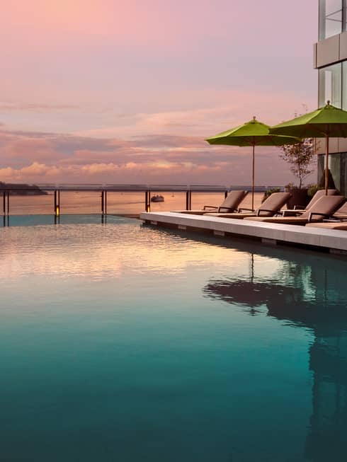 Pink sunset reflected on outdoor swimming pool lined with lounge chairs in front of bay, Seattle Wheel