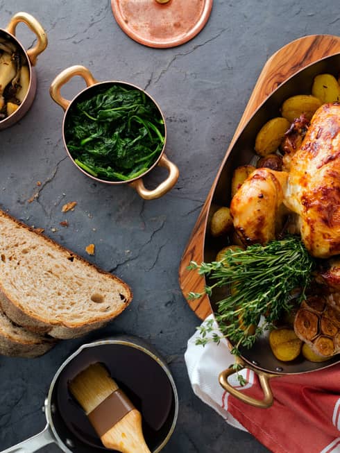 Aerial view of rotisserie whole chicken in roasting pan with herbs, fresh bread