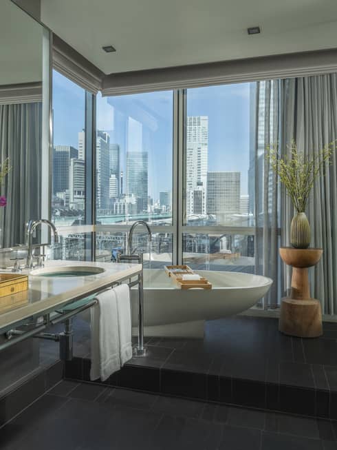 Spacious bathroom with a freestanding bathtub, double-sink vanity and floor-to-ceiling windows offering city views, decorated with flowers