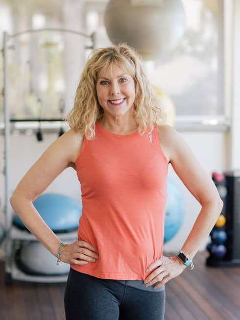 A woman standing in front of exercise balls and large windows.