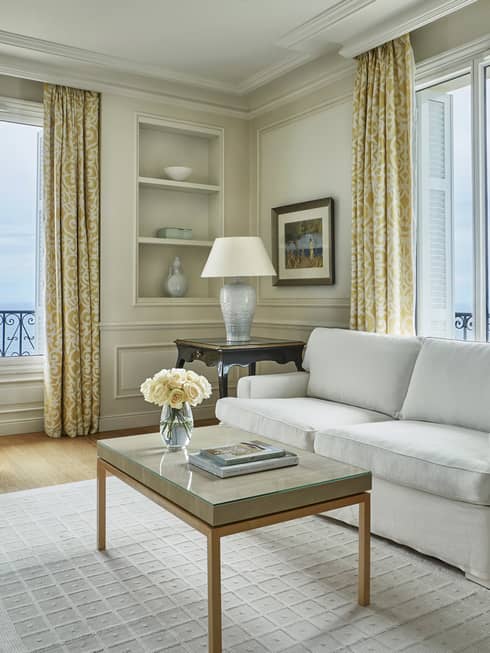 Modern white sofa, armchair, rug, table with books, flowers, corner windows