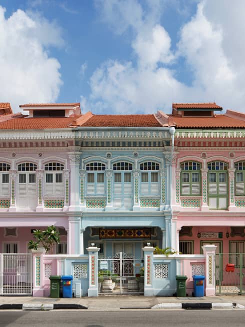 A wide shot of four residential buildings lined up like a rainbow – green, pink and blue with red terracotta roofs.