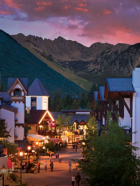 A sunset over a small village like city center with white buildings and mountains in the distance.