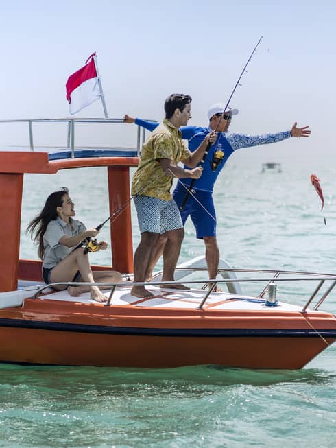 Tour guide teaches two guests to fish on a traditional jukung fishing boat on the open ocean