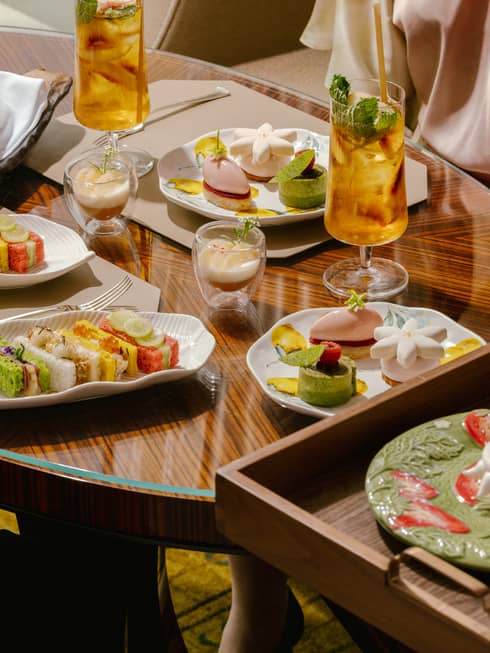A wooden dining table scattered with afternoon tea dishes and drinks