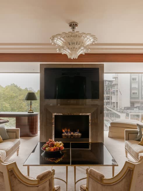 Elegant living room of Presidential Suite, with two sofas and two arm chairs, fireplace, TV and chandelier at Four Seasons Hotel London