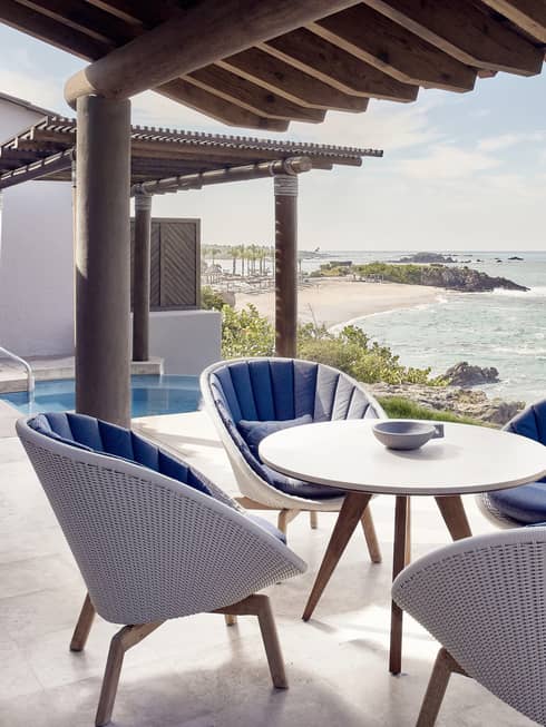 The private outdoor terrace of a modern suite near Puerto Vallarta, with ocean view and plunge pool, featuring a table and four white wicker chairs