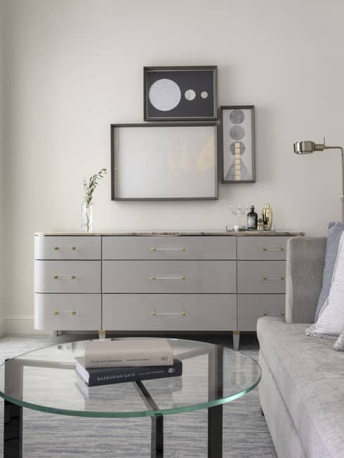 Guest room with silver couch, glass coffee table, grey chest of drawers, and art decor