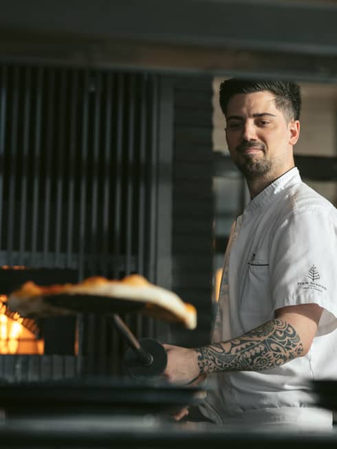 Chef Alessandro de Loe placing a pizza in a large oven