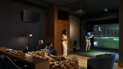 A group of people enjoying an indoor golf simulator experience at the luxury hotel Topgolf Swing Suite, with plush seating and a relaxed atmosphere