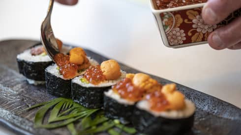A close up of handing garnishing sushi rolls with caviar