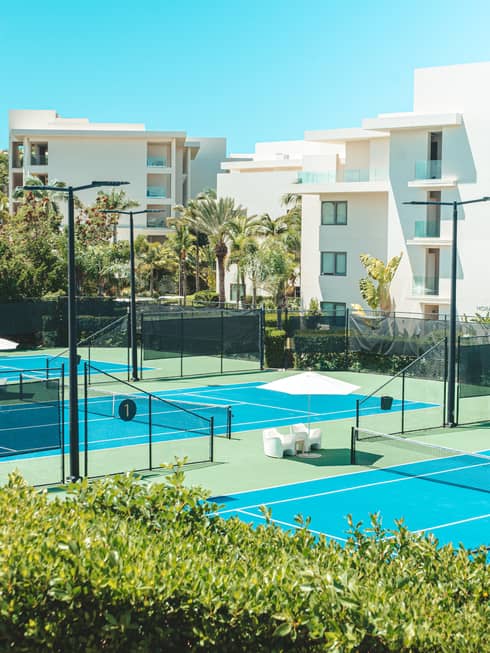 Tennis courts near white buildings and plants.