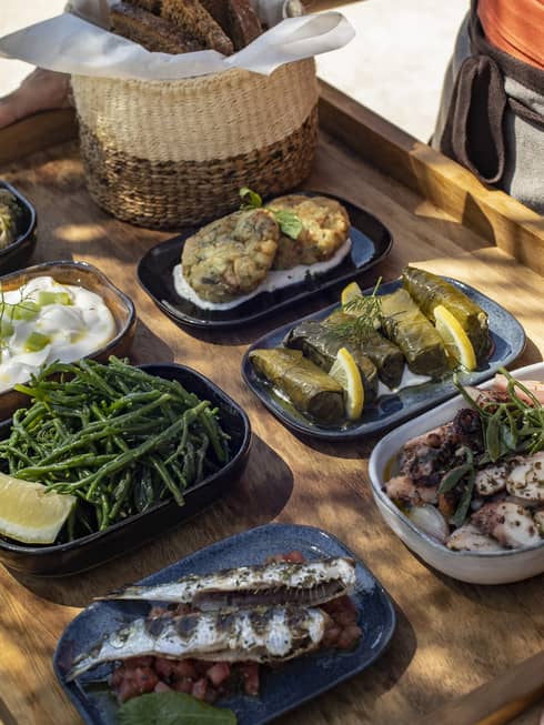 Seven shareable Greek dishes carried on wooden tray outdoors