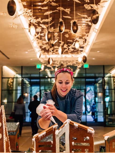 An employee carefully applies icing to an intricate gingerbread house