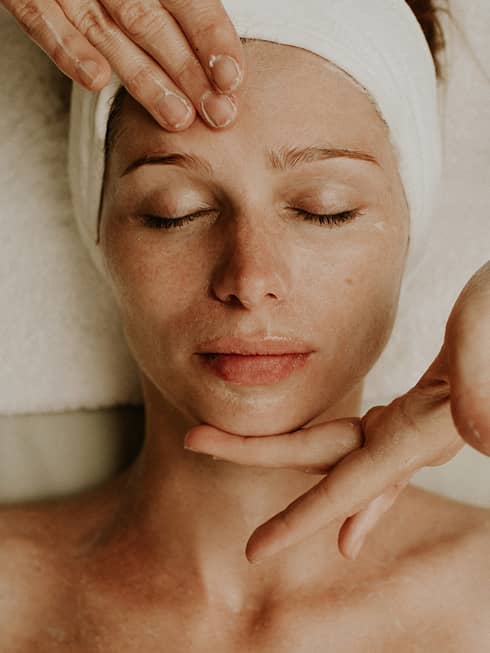 A woman reclines as a spa attendant performs a facial