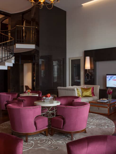 E-Lounge large curved velvet pink chairs around small round tables, modern white spiral staircase in background