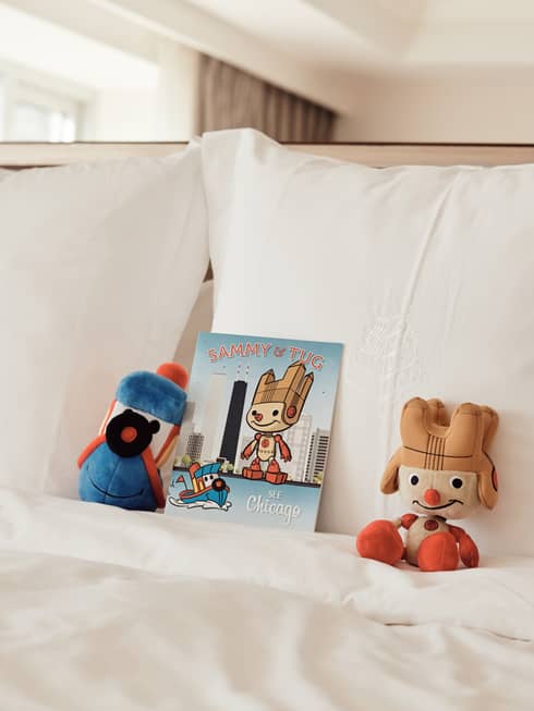 Stuffed animals and a book resting on a white bed.