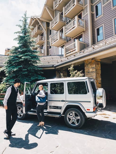 Resort staff opens the driver-side door of a luxury utility vehicle parked in the driveway for guest