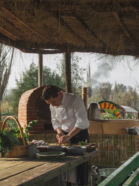 A chef chopping something with a knife outside on an old table, a roof made of old wood covers him.
