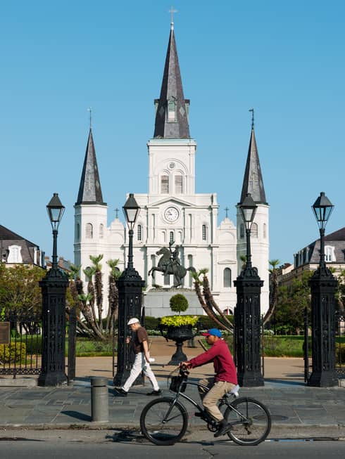 A person riding a bike in front of a large gated building.