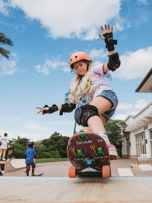 A young girl rides a skateboard at a skate park outside with palm trees