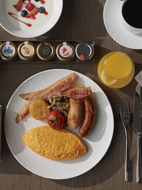 A variety of food on plates including sausage, eggs, fruit, croissant, pastries, jams, and coffee.