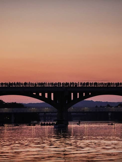Silhouette of people lining long bridge over Lady Bird Lake at sunset
