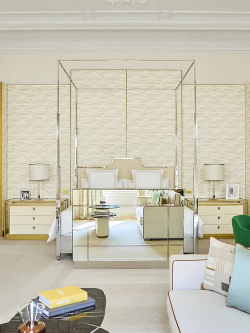 Modern luxury hotel suite with metal four-post bed, dining table with four green chairs, and a sitting area with a white sofa and arm chair