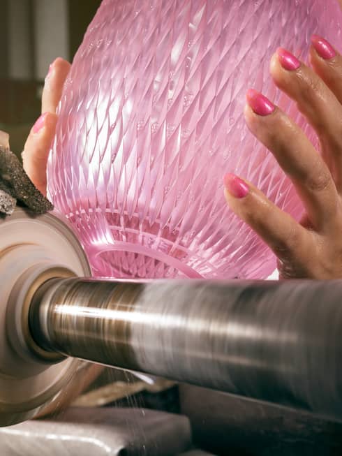 Hands with pink nails hold pink crystal vase atop glass-cutting machine