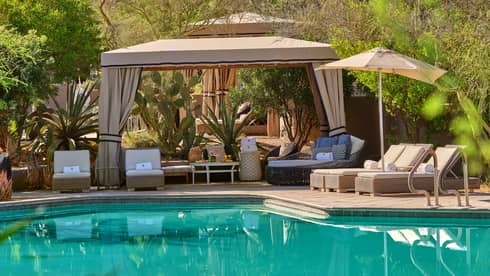 Blue pool with cabana and lounge chairs, surrounded by trees and greenery.