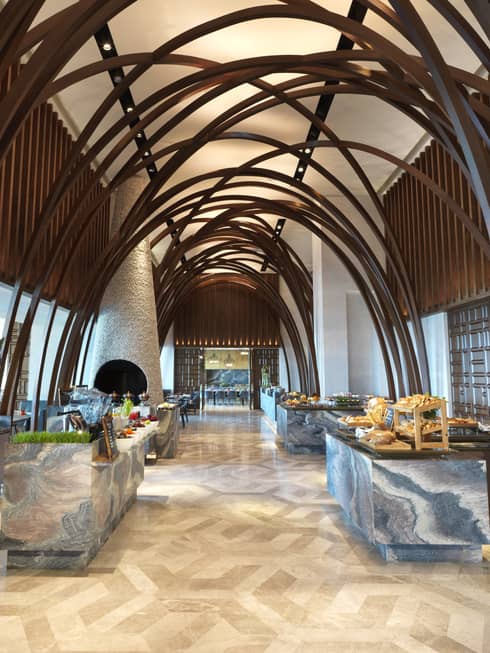 Soaring ceilings, wood arches over marble buffets in modern Arabian Design hallway