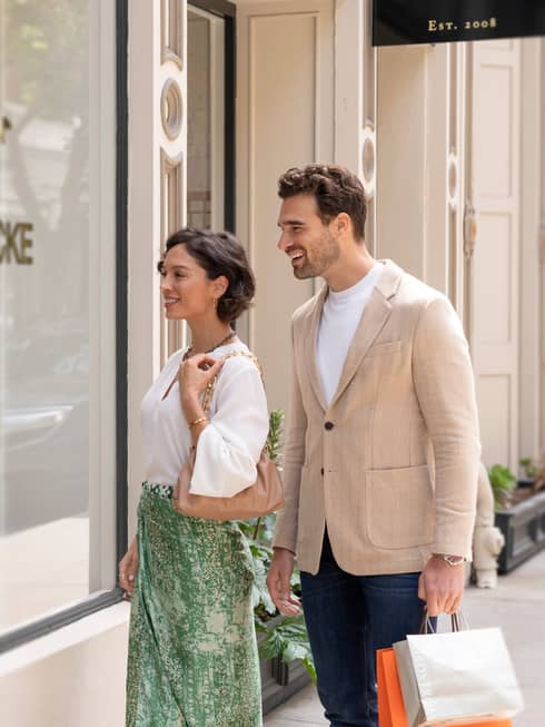 Two people smiling while window shopping in front of a boutique store.
