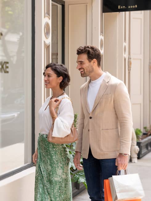 Two people smiling while window shopping in front of a boutique store.