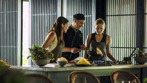 Chef, two women look at pan on kitchen range at Hoi An Cooking Academy 