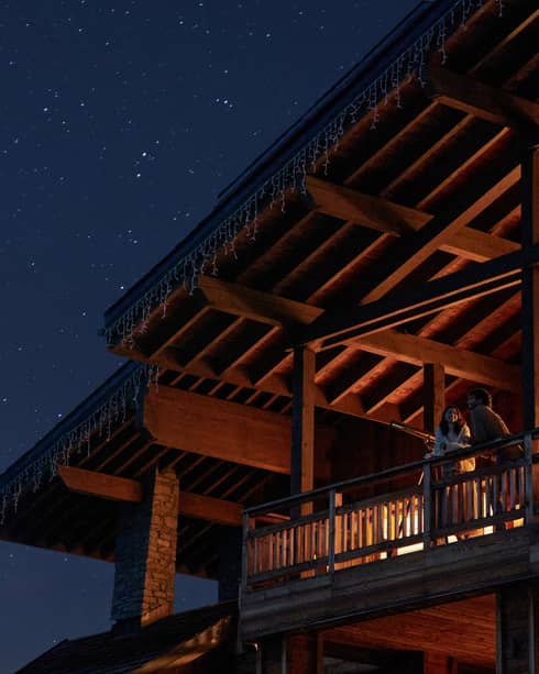 Couple standing on chalet balcony under vaulted ceiling and starry night sky