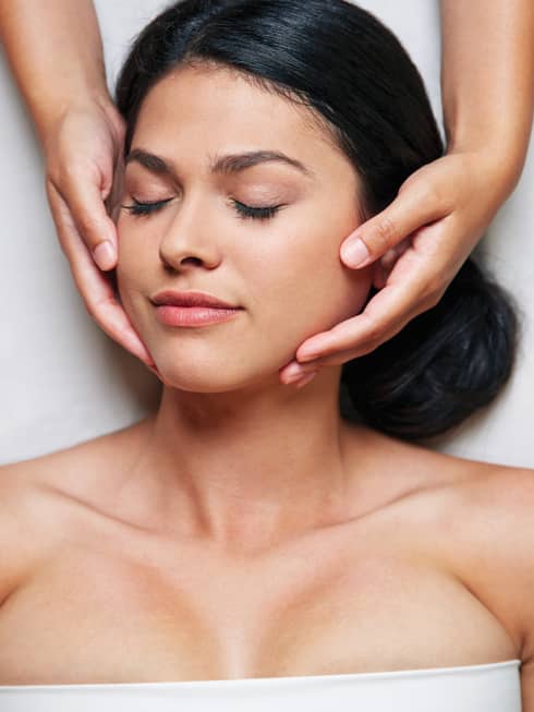 Woman with eyes closed as hands massage her face