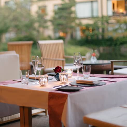 Elegant outdoor dining table set with wine glasses, a small red rose centerpiece and soft lighting at Four Seasons 