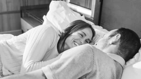 Laughing couple lies together in bed