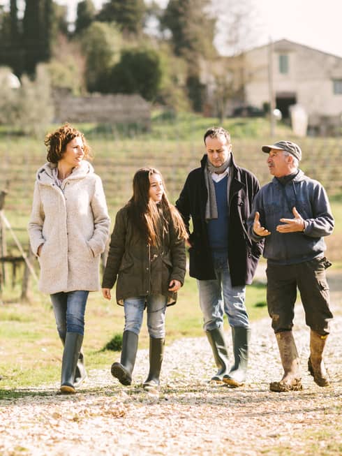 A man and woman, and their two kids walk along a gravel drive on a farm, as the farmer talks to them and uses his hands to communicate
