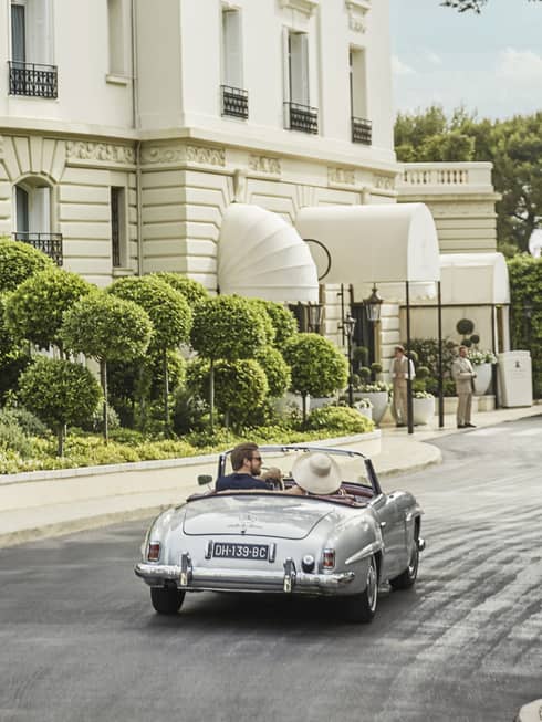 Back view of couple driving luxury convertible bar along sunny city road 