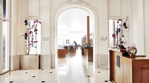 A brightly lit restaurant entrance with cream walls and floor, and a host station made of bright wood.