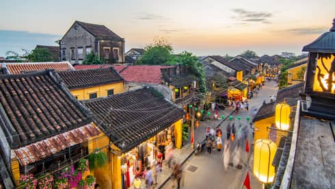 Wood building surrounded by lanterns while people walk on the streets.